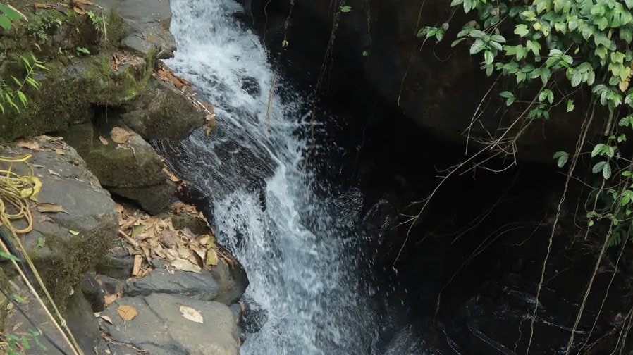 Aerial view of waterfall rushing down mossy rocks into a jungle pool at Holistic Eco-Resort