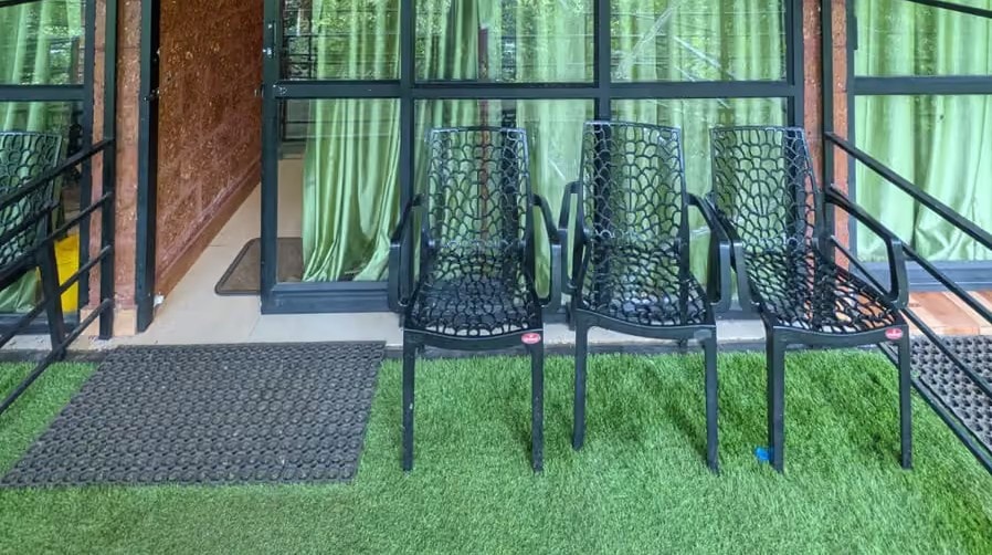 Outdoor balcony seating area with black chairs and green curtains at Holistic Eco-Resort