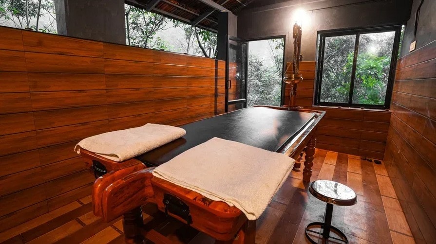 Ayurvedic treatment room with two wooden massage tables and forest views at Holistic Eco-Resort