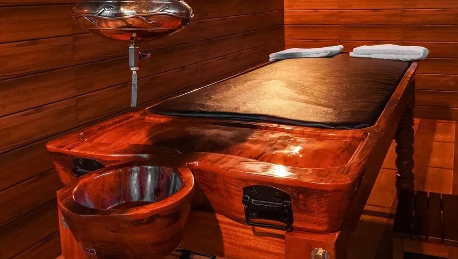 Traditional Ayurvedic Shirodhara treatment table with brass vessel at Holistic Eco-Resort