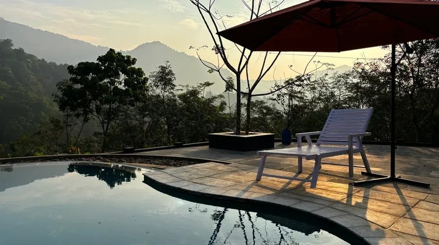 Poolside lounger under a red umbrella with misty mountain views at Holistic Eco-Resort